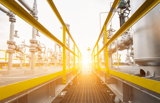 Industrial walkway with yellow railings, pipes, and equipment under bright sunlight